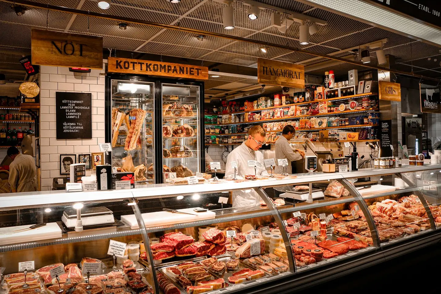 Le comptoir : longue vitrine réfrigérée, carrelage blanc et pièces suspendues en chambre froide