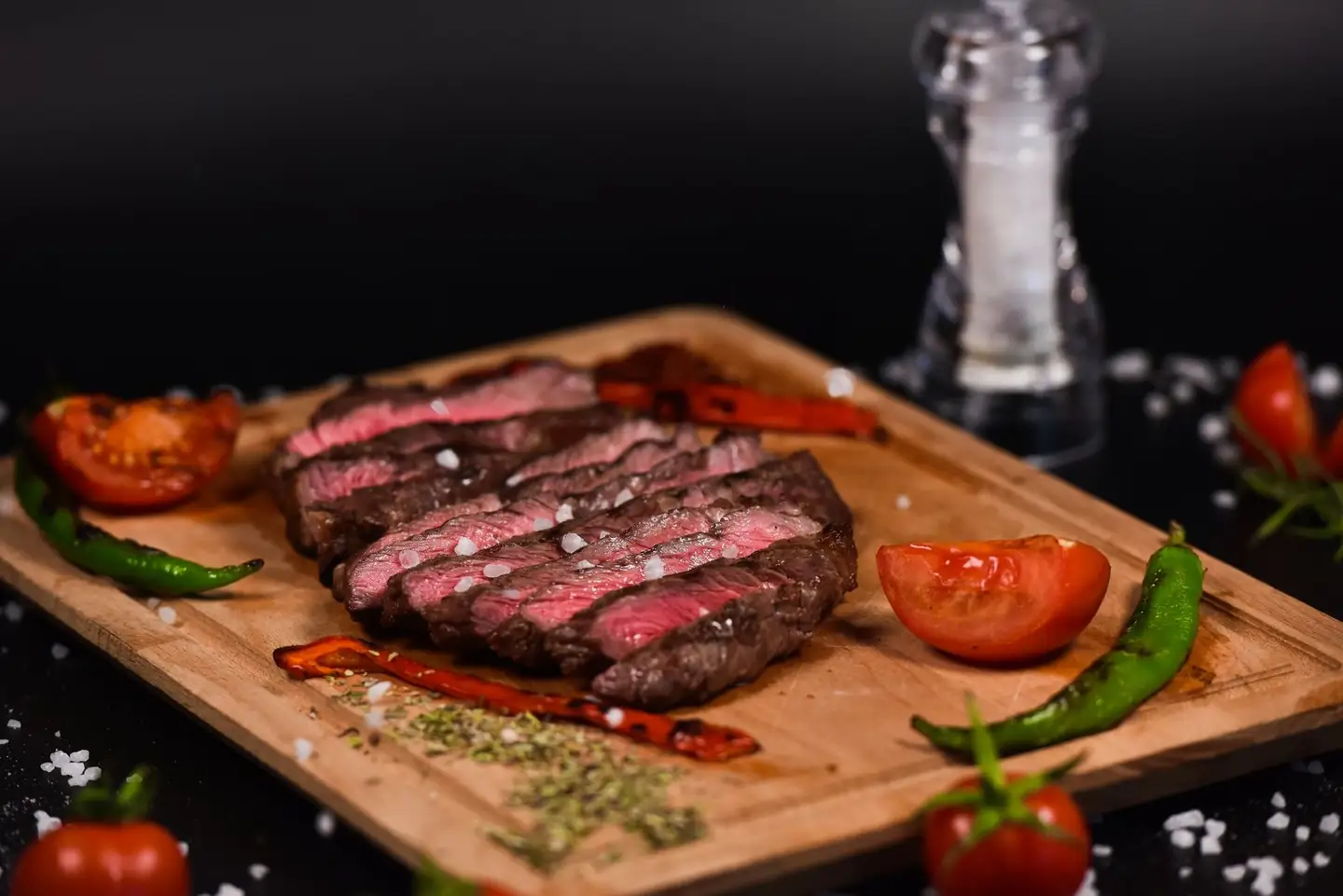 Steak grillé tranché sur la planche, cœur rosé, avec tomates rôties et piments