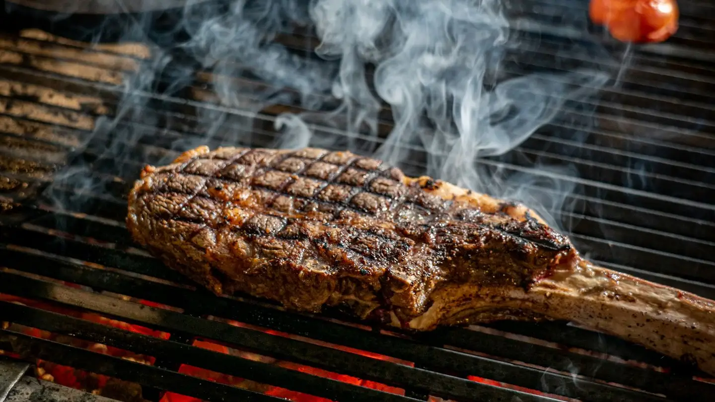 Côte de bœuf tomahawk sur la grille, fumée qui s'élève au-dessus des braises